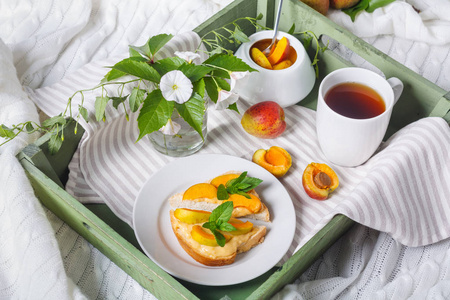 美味的土司面包与自制的杏果酱和杯茶在托盘上, 空心菜的花朵背景