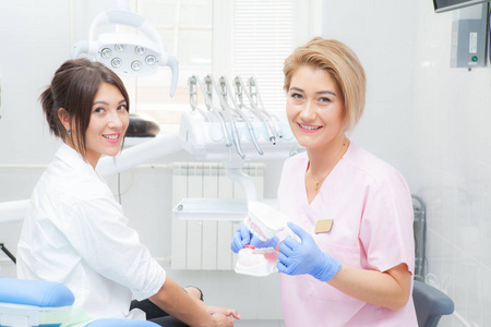 一位女牙医向一位女性病人解释了在模拟上刷牙的过程。都看着摄像机