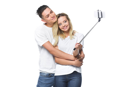 快乐的情侣拍照与智能手机和自拍棒隔离在白色