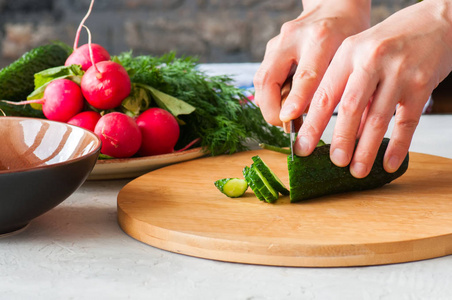 新鲜蔬菜做的健康沙拉。女人的手在木板上切黄瓜。一步法烹饪概念