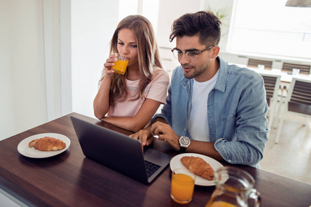 年轻可爱夫妇吃早餐, 而在笔记本电脑浏览