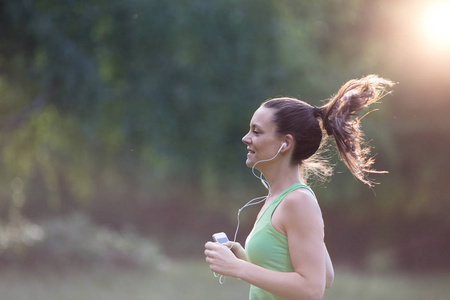 在公园里跑步的戴着耳机的年轻女子的肖像。健康的生活方式概念