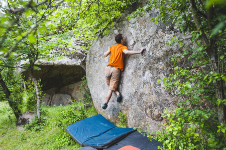 登山者爬上那块石头。运动员从事抱石。在自然攀岩