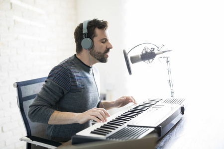 外形视图的好看的拉丁男子与耳机弹钢琴, 唱成麦克风, 唱在线电台节目