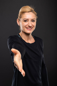 美丽的健身房女教练的肖像提供握手和微笑的黑色背景