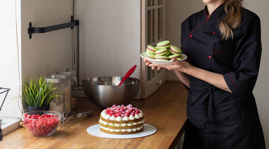糖果在黑色工作制服举行杏仁, 蛋糕与浆果在桌子上。厨房背景。糖果, 蛋糕, 烹饪
