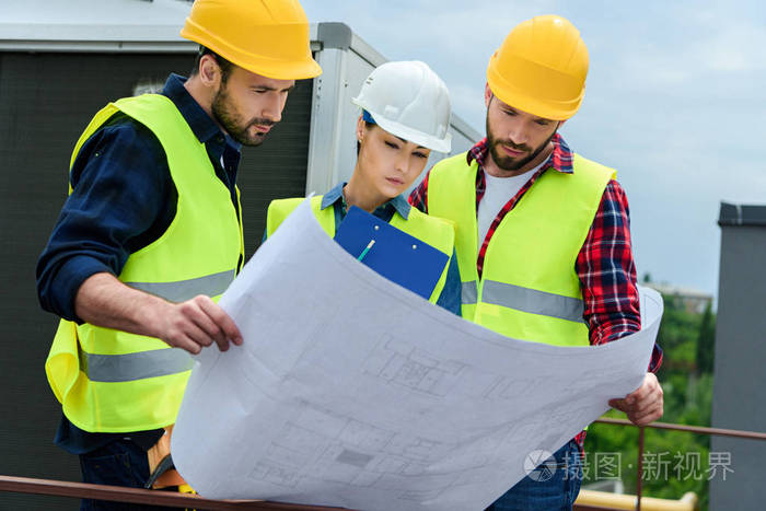hardhats的专业工程师在建筑图纸和剪贴板上工作