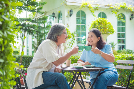 退休的亚洲夫妇坐在餐桌上的花园和喝咖啡