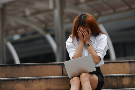 被压力耗尽的年轻的亚洲企业妇女用手在面孔感觉失望或疲乏以工作