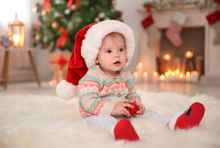 可爱的小宝宝在圣诞老人的帽子坐在毛皮地毯在家里。圣诞庆典