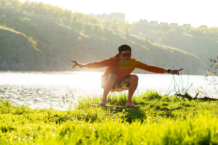 有胡子的人正在平衡板上训练, 在夏日阳光照射下, 在河边的绿色草地上玩耍。后灯, 前视图