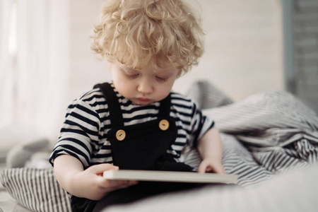 一个金发碧眼的小男孩坐在床上看书。