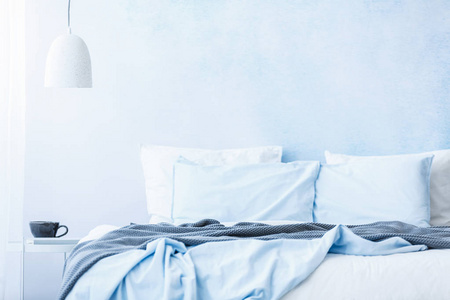 蓝色床单和枕头在床旁边在一张桌与一个杯子在白色灯之下在简单的卧室内部