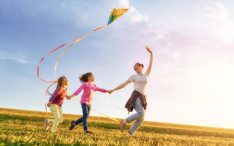 快乐的家庭在户外玩耍。母亲和孩子们跑在草地上, 在夏天的自然风筝