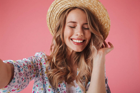 关闭一个可爱的年轻女子的肖像在夏季礼服和草帽采取自拍孤立的粉红色背景