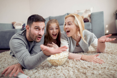 爸爸妈妈和女儿躺在地板上, 看电视, 吃爆米花。