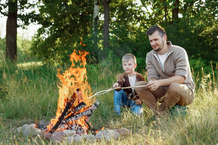 父亲和儿子被火烧在了绿色自然的背景下。远足, 时间与家庭, 家庭生活, 户外消遣