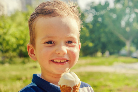 3岁的白种男孩在炎热的夏日里享受融化的冰淇淋。背景绿色夏日树木