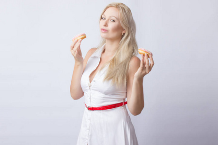 白色礼服的年轻金发女郎手里握着2粉红色的甜甜圈和结霜