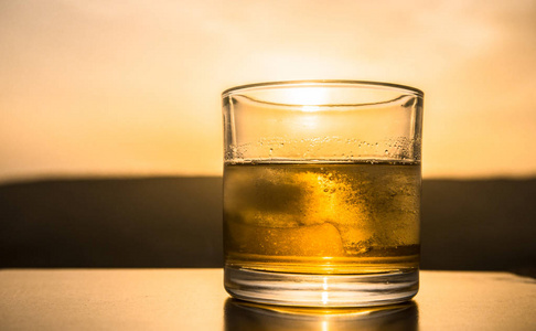 一杯威士忌与冰在日落背景下或拍摄的威士忌在日落戏剧性的天空上的高山景观背景。选择性聚焦