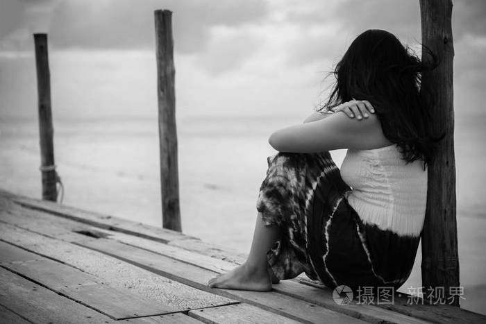 黑色和白色的悲伤和孤独的女人独自坐在一座木桥在海上
