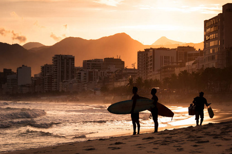 日落时两个冲浪者在海滩上漫步的剪影