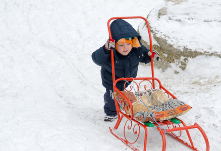 推他的雪橇在雪中的小男孩