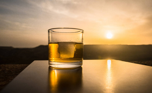 一杯威士忌与冰在日落背景下或拍摄的威士忌在日落戏剧性的天空上的高山景观背景。选择性聚焦