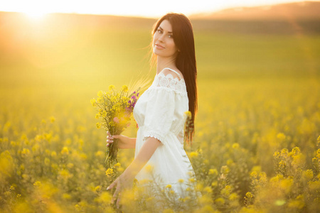 快乐的年轻妇女与花束野花在黄色领域在日落光