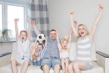 家庭, 体育和娱乐的概念。快乐的母亲父亲女儿和两个儿子足球迷在电视上观看足球比赛, 并在主场庆祝胜利进球。