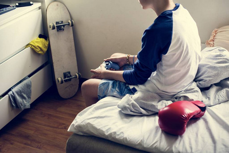 年轻的白种男孩举行游戏控制坐在床上