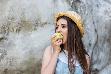 年轻时髦的女人在帽子上吃新鲜的苹果在街上的肖像