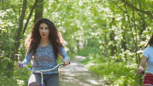 骑自行车的黑发女郎在绿树成荫的背景下骑车, 阳光明媚的一天