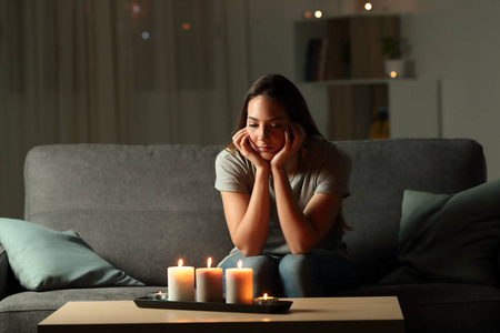 分心的女人看着蜡烛灯停电时坐在客厅的沙发上的家庭