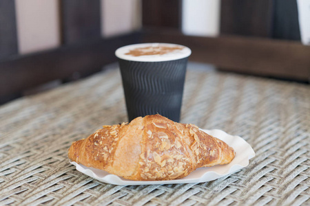 把咖啡放在纸杯里, 用牛角面包放在木桌上。把咖啡放在纸杯里用羊角面包, 合上。选择性聚焦