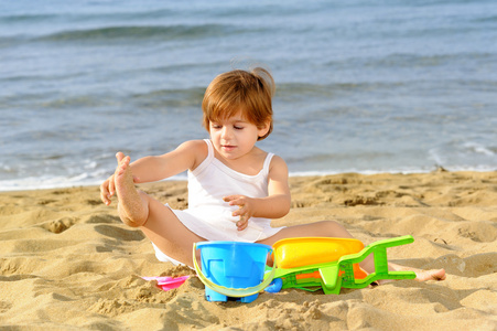 快乐蹒跚学步女孩在海滩上玩她的玩具