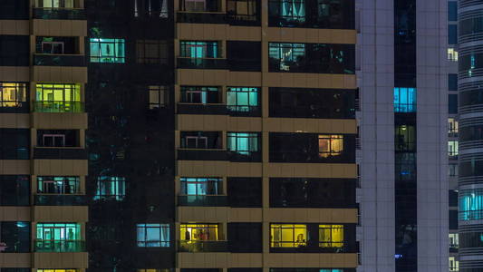 窗户的多层建筑玻璃和钢照明内和移动的人在 timelapse。迪拜现代住宅和办公楼摩天大楼的鸟瞰图。向下平移