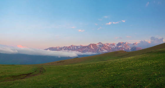 KarachayCherkess 共和国的山脉在日落时有云, 有花的绿草甸