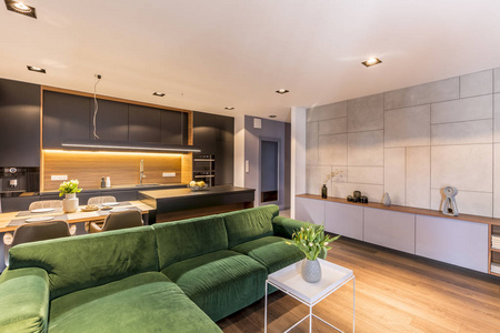 绿色角落沙发在白色桌附近与花在舒适的公寓内部与灰色厨房