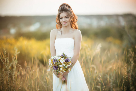 美丽的年轻新娘手持时尚花束的野花在黄色的领域, 自然婚礼的概念