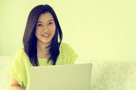 快乐的年轻美丽亚洲女人使用笔记本电脑，室内。复古风格