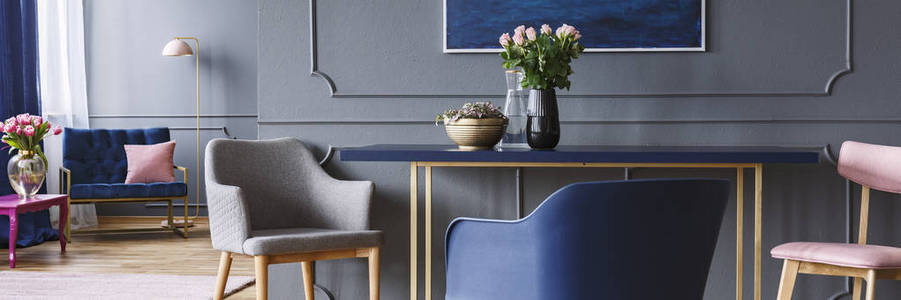 椅子站在蓝色和金色的餐桌上, 粉红色的玫瑰在黑暗的灰色开放空间客厅内部的花瓶