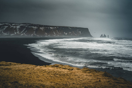 在冰岛著名的黑色沙滩 Reynisfjara 日出。刮风的早晨。海浪。五彩缤纷的天空。早晨日落