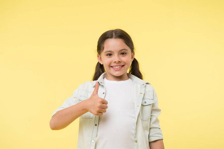快乐的女孩在黄色的背景上竖起大拇指。小孩子用手势微笑。随便看。美丽和时尚。我喜欢这个