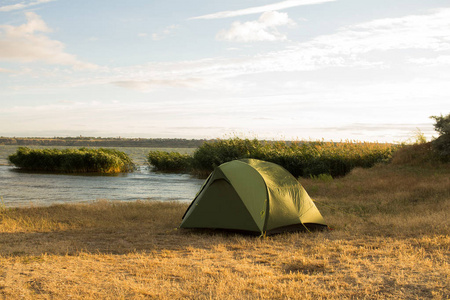 日落或日出时河边远足者的绿色帐篷