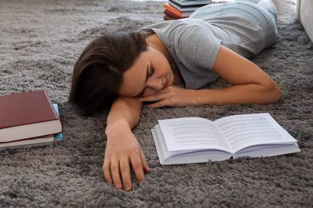 疲倦的年轻妇女与书睡在地毯在家