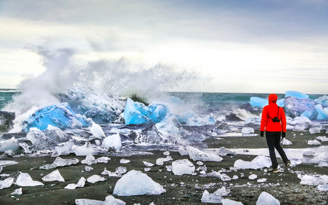 女人看着波浪撞击的反对在 jokulsarlon 冰川环礁湖，冰岛的冰山