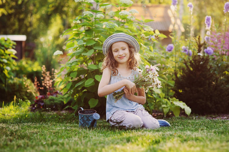快乐的女孩在夏天玩小园丁, 戴着滑稽的帽子, 捧着花束。坐在绿色的草坪上, 享受夏日的户外假期