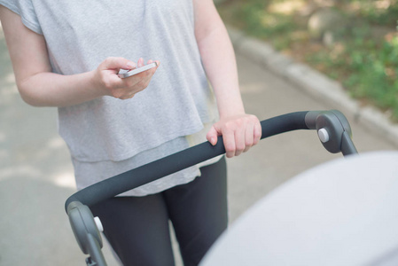 母亲推婴儿推车和阅读短信的智能手机, 而步行在街上休闲运动服装