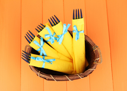 裹在黄色纸餐巾，在柳条篮子里，彩色木制背景上的蓝色塑料叉子